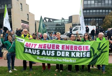sieben Personen halten ein großes Transparent, auf dem steht "Mit neuer Energie raus aus der Krise 'solidariscxherHerbst". Im Hintergrund ist der Eingang des Landtags in Düsseldorf zu sehen