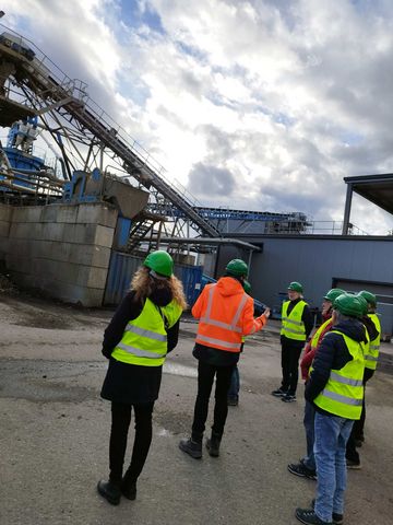 mehrere Personen mit Schutzhelmenstehen vor einer Baustoff-Recyclinganlage