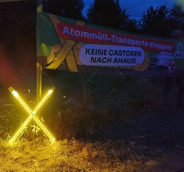 Nachtaufnahme. Transparent "Atommüll-Transporte stoppen. Keine Castoren nach Ahaus", daneben ein gelb leuchtendes X