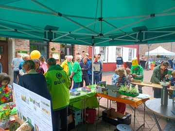 Ansicht eines Infostandes mit mehreren Personen in BUND-Jacken oder T-Shirts. Um den Stand herum stehen mehrere interessierte Erwachsene und Kinder